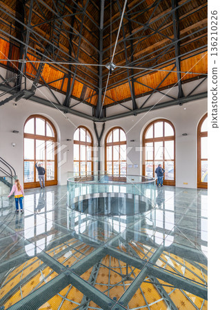 Visitors explore the tower of the National Museum in Prague. The glass floor reveals intricate designs below. Large windows provide views of the city. People engage with the space. Visitors explore the tower of the National Museum in Prague. The glass floor reveals intricate designs below. Large windows provide views of the city. People engage with the space. 136210226
