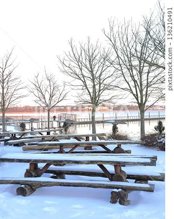 Wooden tables and benches on the lake embankment against the backdrop of sunset. 136210491