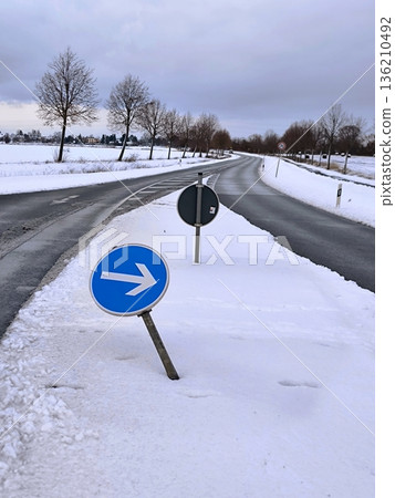 A bent road sign "Turn right" on the snow-covered shoulder of a country road 136210492