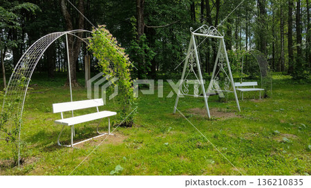 A white bench is in the grass next to a swing 136210835