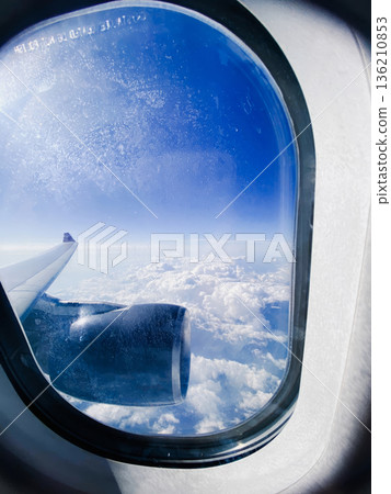 A window on an airplane with a view of the clouds A window on an airplane with a view of the clouds 136210853