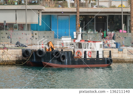 Small harbor workboat moored at quay with tire fenders and deck crane 136211140