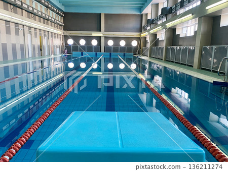 School swimming pool with clear blue water, swim lanes marked by red buoys, and bright lighting creating a serene environment for children's swimming lessons and aquatic activities School swimming pool with clear blue water, swim lanes marked by red buoys, and bright lighting creating a serene environment for children's swimming lessons and aquatic activities 136211274