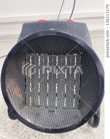 Electric heater with a round design, featuring a metal mesh front and heating elements, positioned on a smooth surface, showcasing modern heating technology for indoor comfort 136211279