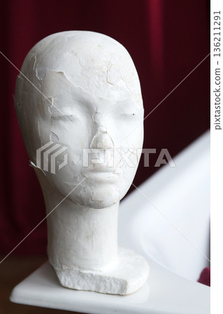 White plaster mannequin head with cracked surface texture, positioned on a white surface, showcasing artistic details and unique design elements in a creative environment 136211291
