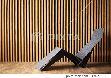 Modern lounge chair with sleek design, crafted from gray felt and wood, positioned against a textured wooden wall, showcasing contemporary interior aesthetics and comfort Modern lounge chair with sleek design, crafted from gray felt and wood, positioned against a textured wooden wall, showcasing contemporary interior aesthetics and comfort 136211315