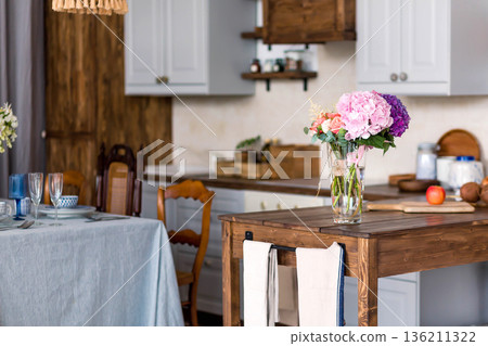 Bright and inviting kitchen interior featuring a wooden table with a vase of colorful flowers, elegant dining setup, and warm ambiance for a cozy home atmosphere 136211322