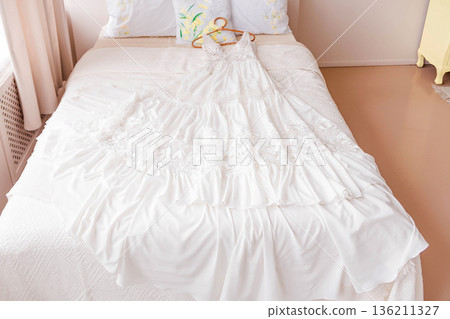 Elegant wedding dress displayed on a neatly made bed, showcasing intricate lace details and soft fabric, symbolizing the anticipation of a beautiful wedding day Elegant wedding dress displayed on a neatly made bed, showcasing intricate lace details and soft fabric, symbolizing the anticipation of a beautiful wedding day 136211327