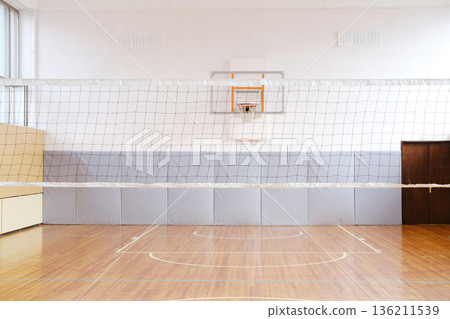 Indoor volleyball court featuring a net, wooden flooring, and padded walls, creating a spacious environment for sports activities and athletic training sessions Indoor volleyball court featuring a net, wooden flooring, and padded walls, creating a spacious environment for sports activities and athletic training sessions 136211539