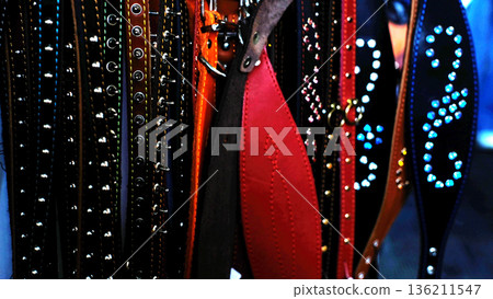 Animal collars in various colors and materials displayed on rack with studs and embellishments, including black, brown, red, and blue collars hanging side by side in close proximity Animal collars in various colors and materials displayed on rack with studs and embellishments, including black, brown, red, and blue collars hanging side by side in close proximity 136211547