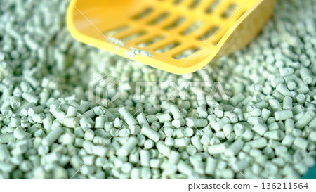 Green tea cat litter with a yellow scoop on a textured surface, showcasing eco-friendly materials and providing a clean, natural environment for pets with copy space 136211564