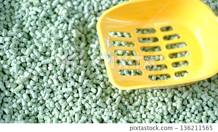 Green pellets scattered on a surface with a yellow scoop resting atop, showcasing texture and color contrast in a vibrant and engaging composition for various applications 136211565