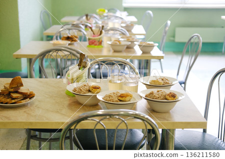 School cafeteria setting with tables arranged for lunch, featuring nutritious meals in bowls, promoting healthy eating habits for children and fostering well-being in educational environments School cafeteria setting with tables arranged for lunch, featuring nutritious meals in bowls, promoting healthy eating habits for children and fostering well-being in educational environments 136211580