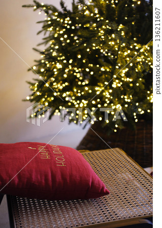 Cozy Christmas living room decor featuring a minimalist Scandinavian style with a beautifully lit tree and a festive pillow, creating a warm holiday atmosphere with copy space Cozy Christmas living room decor featuring a minimalist Scandinavian style with a beautifully lit tree and a festive pillow, creating a warm holiday atmosphere with copy space 136211607