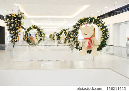 Christmas decorations featuring festive wreaths and plush teddy bears in a modern shopping center, creating a joyful holiday atmosphere with vibrant colors and cheerful ambiance 136211613