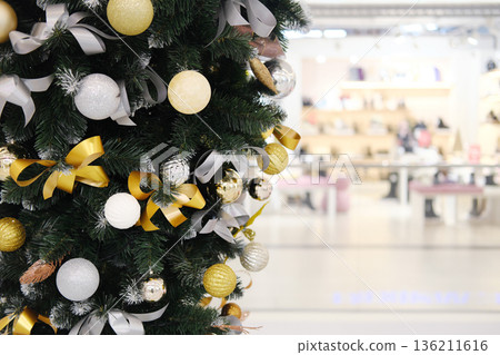 Christmas tree adorned with golden and silver ornaments, ribbons, and baubles, creating a festive atmosphere in a vibrant shopping center with blurred background Christmas tree adorned with golden and silver ornaments, ribbons, and baubles, creating a festive atmosphere in a vibrant shopping center with blurred background 136211616
