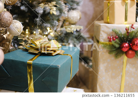 Festively wrapped green gift box with golden ribbon and bow, surrounded by decorated Christmas tree and other presents, creating a joyful holiday atmosphere Festively wrapped green gift box with golden ribbon and bow, surrounded by decorated Christmas tree and other presents, creating a joyful holiday atmosphere 136211655