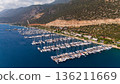 Drone aerial view of a coastal marina filled with yachts and boats near mountains and shoreline. Calm sea water, resort area, summer travel destination. 136211669