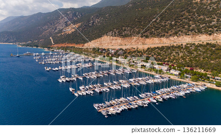 Drone aerial view of a coastal marina filled with yachts and boats near mountains and shoreline. Calm sea water, resort area, summer travel destination. Drone aerial view of a coastal marina filled with yachts and boats near mountains and shoreline. Calm sea water, resort area, summer travel destination. 136211669