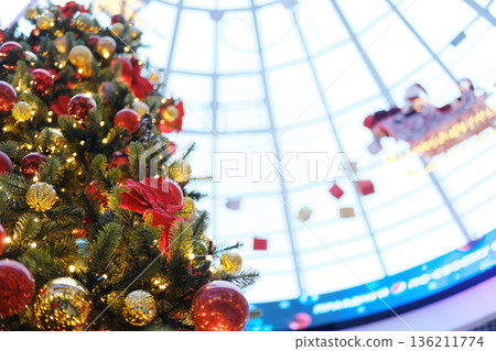 Christmas tree adorned with vibrant ornaments and lights, towering under a glass dome in a festive shopping mall, creating a magical holiday atmosphere Christmas tree adorned with vibrant ornaments and lights, towering under a glass dome in a festive shopping mall, creating a magical holiday atmosphere 136211774