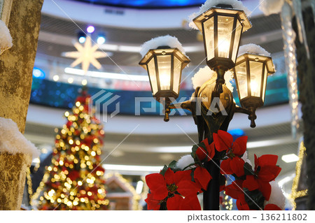 Christmas decorations featuring a charming fairytale town scene in a shopping mall, with illuminated street lamps, festive trees, and vibrant holiday colors creating a magical atmosphere Christmas decorations featuring a charming fairytale town scene in a shopping mall, with illuminated street lamps, festive trees, and vibrant holiday colors creating a magical atmosphere 136211802