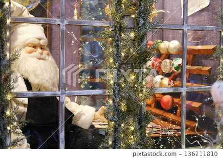 Festive Christmas window display featuring a lifelike Santa Claus surrounded by colorful ornaments and twinkling lights, creating a joyful holiday atmosphere in a shopping mall Festive Christmas window display featuring a lifelike Santa Claus surrounded by colorful ornaments and twinkling lights, creating a joyful holiday atmosphere in a shopping mall 136211810