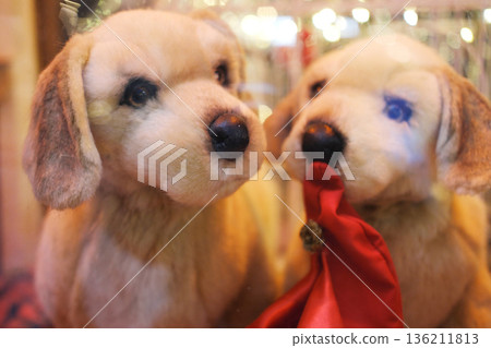 Two adorable plush dogs with soft fur and expressive eyes, holding a red gift bag, create a festive atmosphere in a decorated shopping mall during the holiday season Two adorable plush dogs with soft fur and expressive eyes, holding a red gift bag, create a festive atmosphere in a decorated shopping mall during the holiday season 136211813