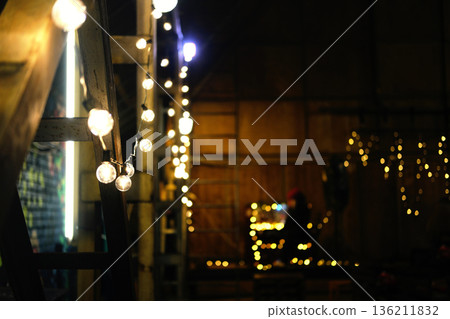 Warmly lit Christmas decorations with glowing string lights and festive ambiance creating a cozy atmosphere for holiday celebrations and gatherings in a rustic setting 136211832