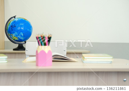Classroom setting featuring a globe and colorful pencils in a pink holder on a wooden desk, with open books and copy space for educational themes Classroom setting featuring a globe and colorful pencils in a pink holder on a wooden desk, with open books and copy space for educational themes 136211861