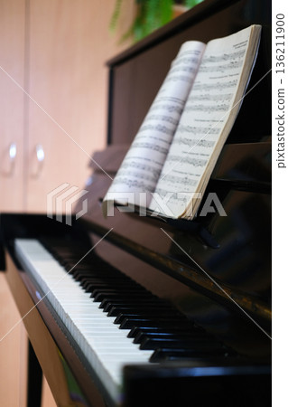 Black piano with sheet music open on the stand, showcasing the keys and polished surface, surrounded by a warm and inviting interior atmosphere for musical inspiration Black piano with sheet music open on the stand, showcasing the keys and polished surface, surrounded by a warm and inviting interior atmosphere for musical inspiration 136211900