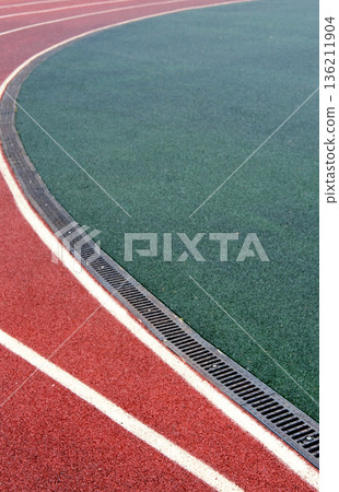 Curved track surface featuring vibrant red and green colors, showcasing athletic field design with white lane markings and drainage system for sports activities Curved track surface featuring vibrant red and green colors, showcasing athletic field design with white lane markings and drainage system for sports activities 136211904