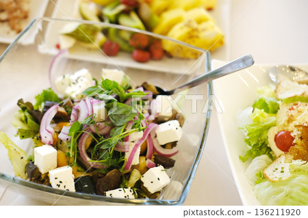 Fresh salad featuring vibrant greens, colorful vegetables, and feta cheese, served in a clear glass bowl, showcasing healthy eating and culinary presentation Fresh salad featuring vibrant greens, colorful vegetables, and feta cheese, served in a clear glass bowl, showcasing healthy eating and culinary presentation 136211920