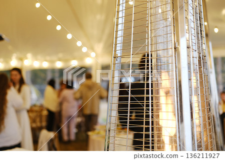 Heat gun providing warmth in a tent during a cold weather event, creating a cozy atmosphere for guests enjoying the gathering and enhancing comfort levels 136211927