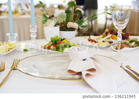 Elegant dining table setting with fine glassware, decorative plates, fresh vegetables, and floral centerpiece, creating a sophisticated atmosphere for special occasions 136211945