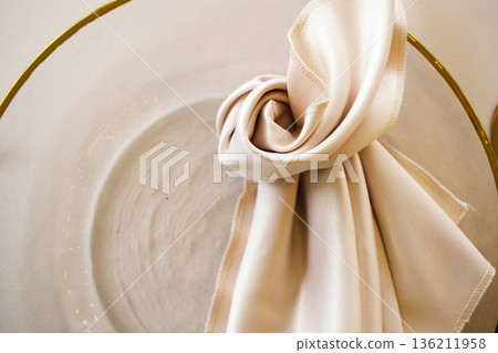 Elegant folded fabric napkin in a circular glass bowl with a gold rim, showcasing sophisticated table setting and modern dining aesthetics for upscale events Elegant folded fabric napkin in a circular glass bowl with a gold rim, showcasing sophisticated table setting and modern dining aesthetics for upscale events 136211958