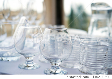 Clear glassware collection featuring elegant stemmed glasses and simple tumblers arranged on a table, showcasing transparency and reflections in a bright setting Clear glassware collection featuring elegant stemmed glasses and simple tumblers arranged on a table, showcasing transparency and reflections in a bright setting 136211965
