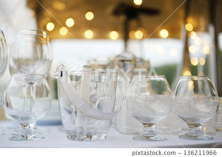 Elegant glass tableware arranged for a festive celebration, featuring a variety of drinkware and an ice bucket, creating a sophisticated atmosphere for special events 136211966