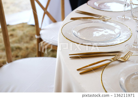 Elegant wedding table setting with gold cutlery and clear plates, featuring soft textures and natural elements, perfect for holiday celebrations and special occasions with copy space Elegant wedding table setting with gold cutlery and clear plates, featuring soft textures and natural elements, perfect for holiday celebrations and special occasions with copy space 136211971