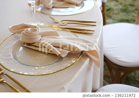 Elegant dining table setting featuring fine china plates, golden cutlery, and soft fabric napkins, creating a sophisticated atmosphere for special occasions and gatherings 136211972