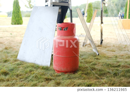 Red gas cylinder positioned on grass near a heat gun setup, showcasing preparation for an event with tools and equipment ready for use in a professional environment 136211985