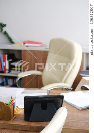 Modern office workspace featuring a stylish ergonomic chair, tablet on desk, organized paperwork, and vibrant greenery, creating a productive and inviting atmosphere for professionals Modern office workspace featuring a stylish ergonomic chair, tablet on desk, organized paperwork, and vibrant greenery, creating a productive and inviting atmosphere for professionals 136212007