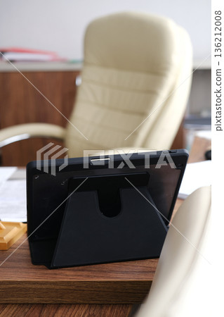 Black tablet on a wooden desk with a sleek stand, surrounded by office supplies and a modern chair, creating a professional workspace atmosphere for productivity Black tablet on a wooden desk with a sleek stand, surrounded by office supplies and a modern chair, creating a professional workspace atmosphere for productivity 136212008