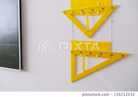 Yellow geometric tools including protractors and rulers are displayed on a classroom wall next to a chalkboard, emphasizing the importance of geometry in school education Yellow geometric tools including protractors and rulers are displayed on a classroom wall next to a chalkboard, emphasizing the importance of geometry in school education 136212010