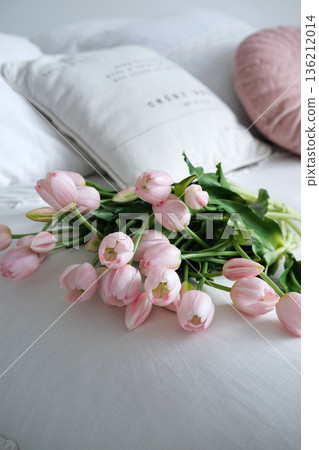 Pink tulips arranged beautifully on a soft white bedspread, with decorative pillows in the background, creating a serene and inviting atmosphere for relaxation and comfort 136212014