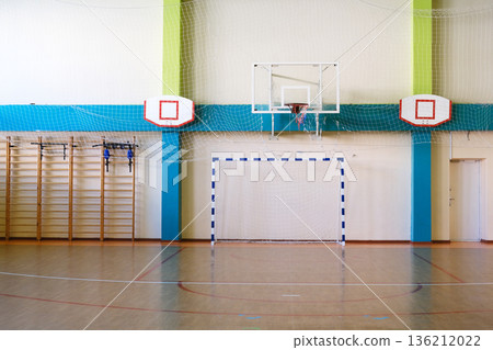 Empty school gym interior featuring basketball hoop and handball goal, showcasing spacious wooden floor and colorful walls with copy space for design purposes Empty school gym interior featuring basketball hoop and handball goal, showcasing spacious wooden floor and colorful walls with copy space for design purposes 136212022