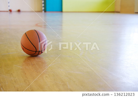 Basketball resting on polished wooden gym floor, surrounded by vibrant colored walls, representing sports education and physical activity in school environments 136212023