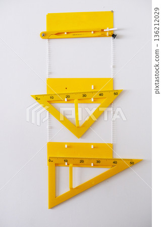 Yellow drafting tools including a protractor and triangle rulers arranged vertically on a white background, showcasing precision measurement and design elements in a creative workspace Yellow drafting tools including a protractor and triangle rulers arranged vertically on a white background, showcasing precision measurement and design elements in a creative workspace 136212029