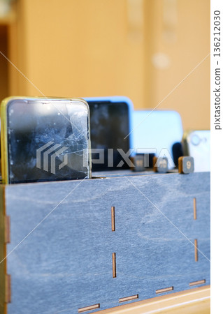 Students' smartphones stored in a wooden box, showcasing a ban on cell phones in school, promoting focus and engagement in educational environments with copy space 136212030