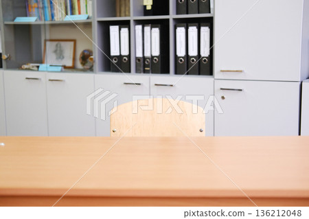 Empty wooden chair at a school desk in a classroom setting, surrounded by organized shelves filled with binders and educational materials, creating a focused learning environment Empty wooden chair at a school desk in a classroom setting, surrounded by organized shelves filled with binders and educational materials, creating a focused learning environment 136212048