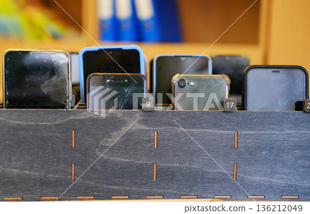 Collection of students' cell phones stored in a wooden box, showcasing various models and conditions, emphasizing the importance of device management in educational environments Collection of students' cell phones stored in a wooden box, showcasing various models and conditions, emphasizing the importance of device management in educational environments 136212049
